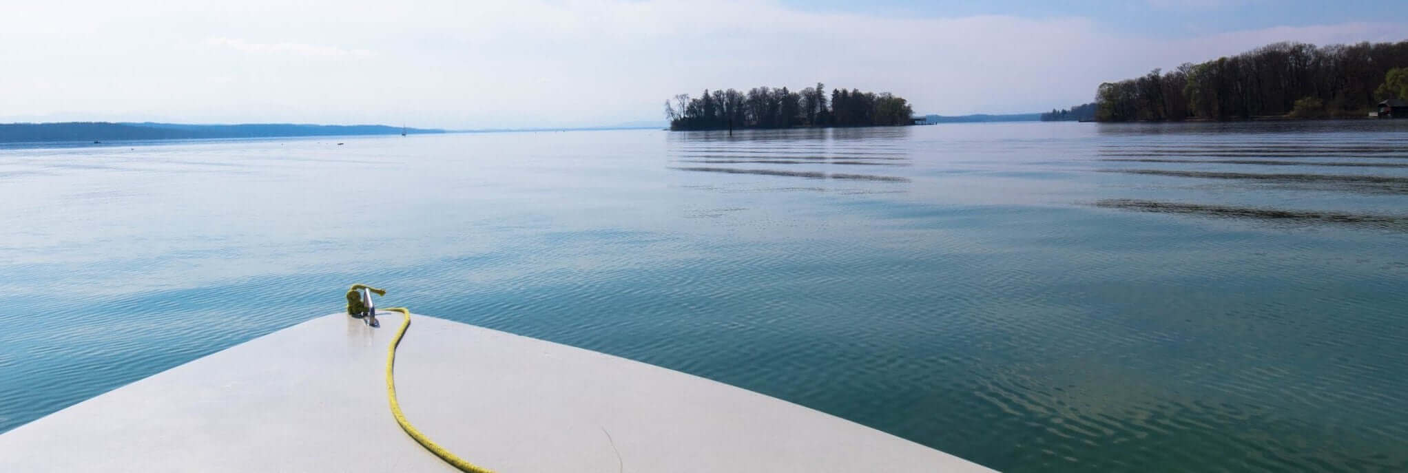 Bootsverleih & Elektroboote: Aussicht von einem Boot auf den ruhigen See und die Insel im Hintergrund.